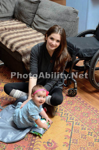 image of a young mother sitting on floor playing with her baby with a wheelchair beside her