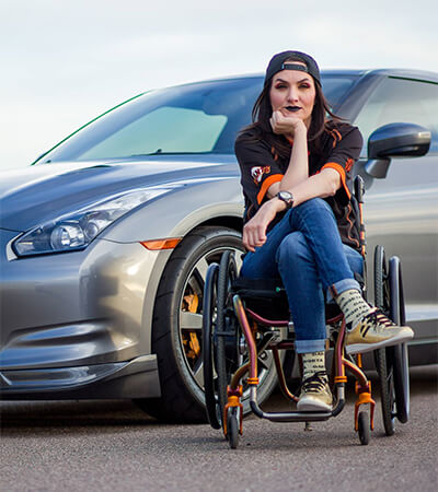 Gina sitting on a wheelchair wearing jeans and t shirt with black lipstick