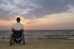 image of a man sitting on a wheelchair at beach looking at the sky