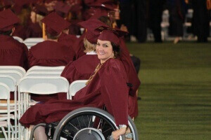 a girl on a wheelchair wearing maroon graduation gown and cap