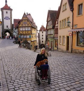 Kelly in courtyard in Rothenburg, Germany in her "cobblestone chair" that her husband outfitted with big wheels and castors.
