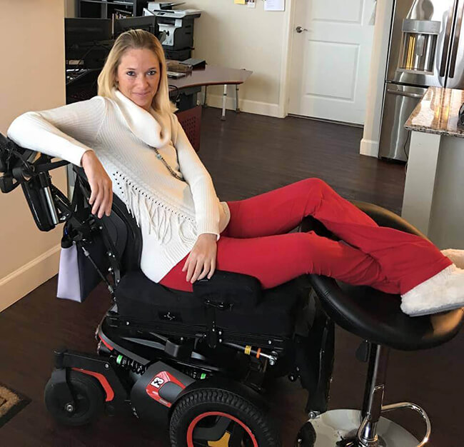 Ali seen in an electric wheelchair posing in red pants and white sweater