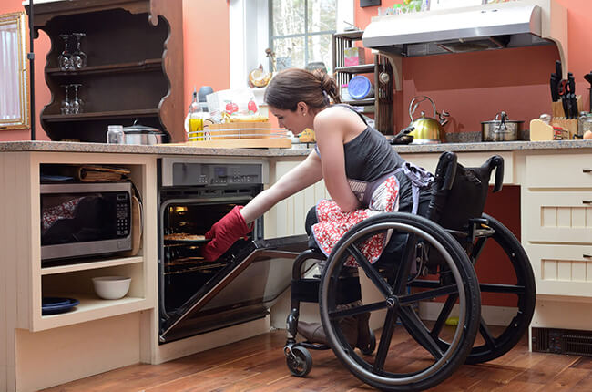 Woman in wheelchair taking tray out of oven