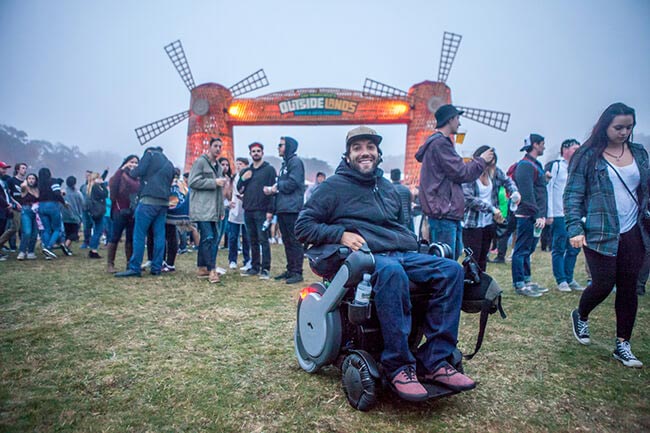 man shown at an outdoor festival smiling in an electric WHILL wheelchair