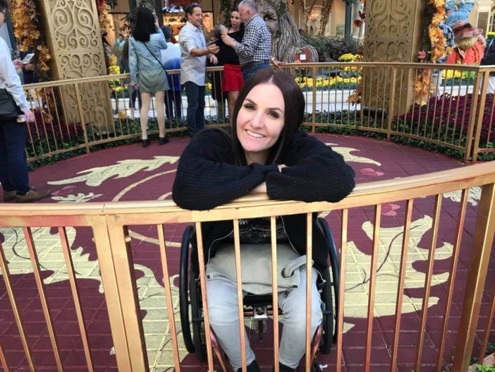 Gina shown sitting in wheelchair smiling while behind a gated circle made of gold in a out door mall
