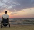 man sitting in wheelchair watching sunrise on a beach