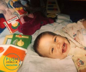 Courtney 8 300x253 - A baby girl smiling while lying on a bed surrounded by toys and books